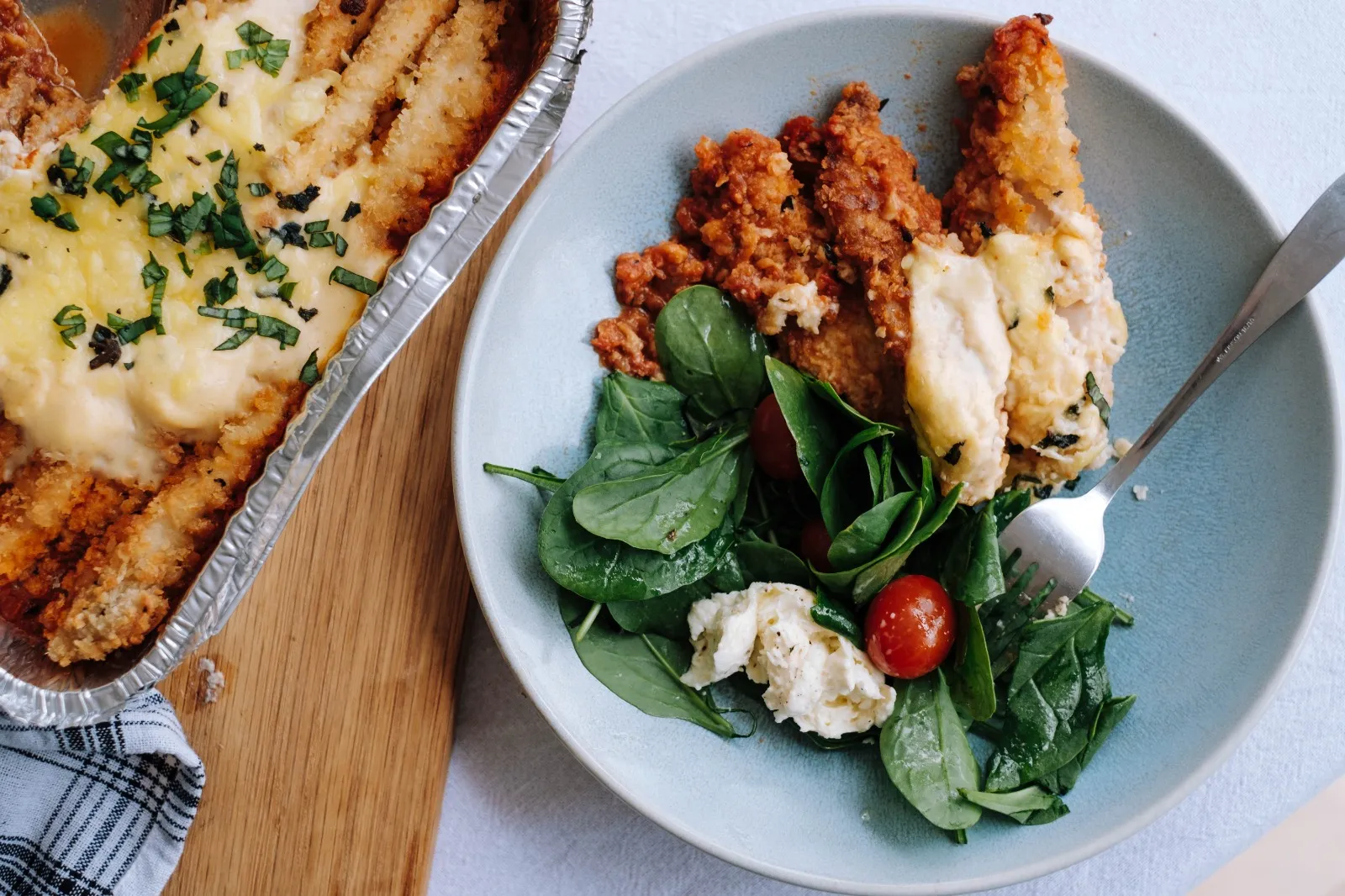 Chicken parmesan meal in foil container with plated portion and fresh salad